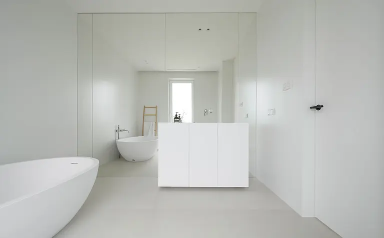 Nowoczesna łazienka z minimalistycznym designem, biała wanna, lustro i szare ściany.