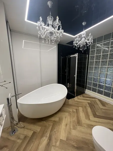 Nowoczesna łazienka z białą wanną, szklanym prysznicem i kryształowymi żyrandolami w stylu glamour.