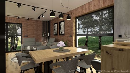 Wnętrze salonu w stylu industrialnym z drewnianym stołem, szarymi fotelami i ceglaną ścianą.