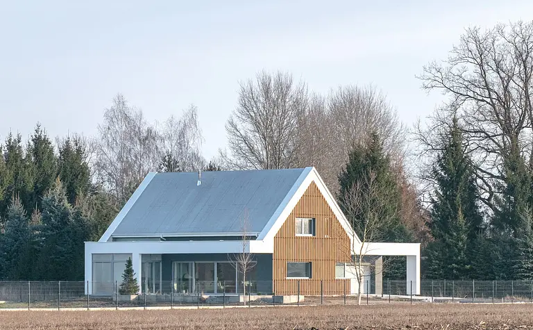 Nowoczesny dom z drewnianą elewacją i dużymi oknami pośród natury.