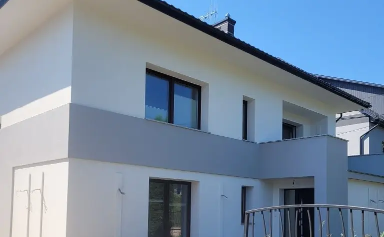 Nowoczesny dom z szarymi elementami i dużymi oknami, minimalistyczny styl.