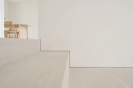 Minimalistyczne schody z jasnym drewnem prowadzące do białego wnętrza