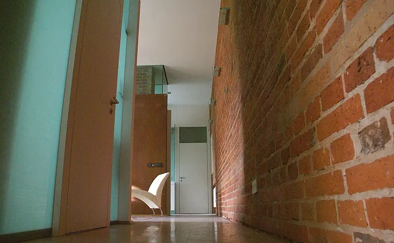 Korytarz w stylu eklektycznym i industrialnym z ceglaną ścianą i nowoczesnymi drzwiami.