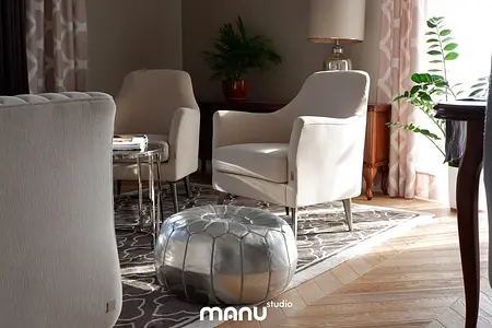 Eleganckie wnętrze salonu z jasnymi fotelami, metalowym pufem i rośliną. Styl tradycyjny.