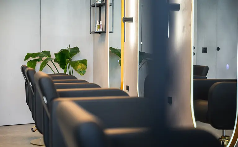 Wnętrze salonu fryzjerskiego z czarnymi fotelami i roślinami, styl industrialny i współczesny