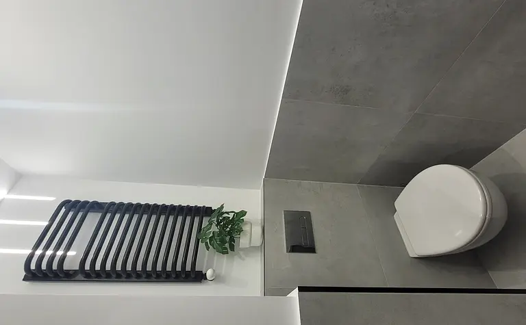 Minimalistyczna toaleta z szarymi płytkami i białą miską.