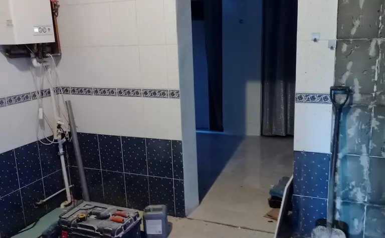Wnętrze kuchni z białymi płytkami, niebieskimi akcentami i narzędziami budowlanymi.