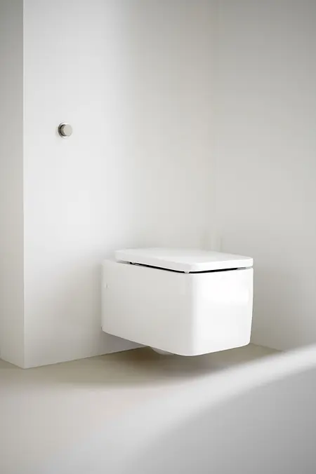 Minimalistyczna łazienka z nowoczesną toaletą i ścianami w kolorze białym.