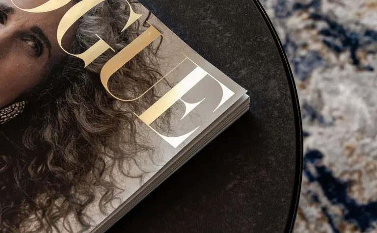 Stolik kawowy z magazynem Vogue na ciemnym stole w nowoczesnym wnętrzu.