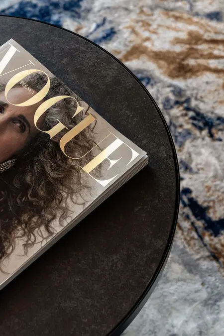 Stolik kawowy z magazynem Vogue na ciemnym stole w nowoczesnym wnętrzu.