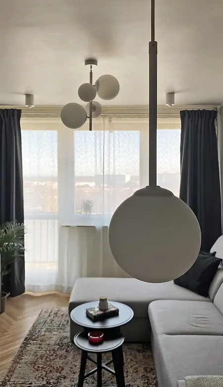Wnętrze salonu w stylu eklektycznym z minimalistycznymi akcentami, nowoczesnym oświetleniem i vintage'owym dywanem.