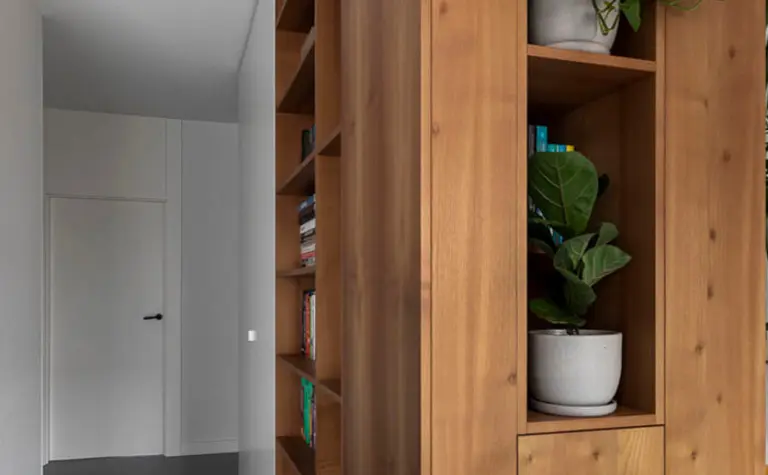 Korytarz z minimalistycznym wystrojem, drewnianą półką i nowoczesnymi roślinami.