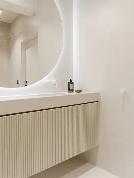 Minimalistyczna łazienka w stylu japandi z białą umywalką i oświetleniem LED.