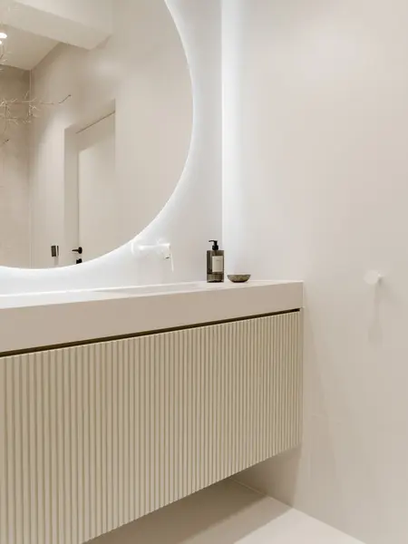 Minimalistyczna łazienka w stylu japandi z białą umywalką i oświetleniem LED.