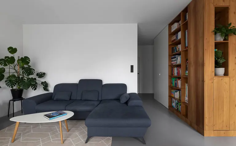 Minimalistyczny salon z niebieską kanapą, drewnianą biblioteczką i rośliną.