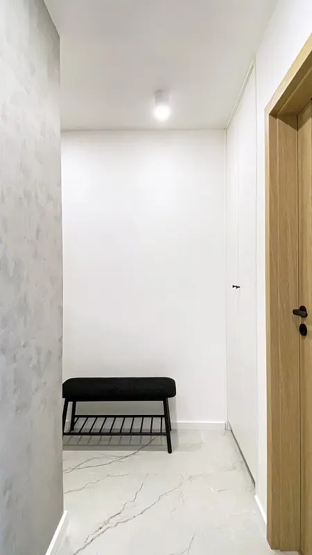 Przedpokój w stylu eklektycznym i minimalistycznym z białymi ścianami i czarną ławką.