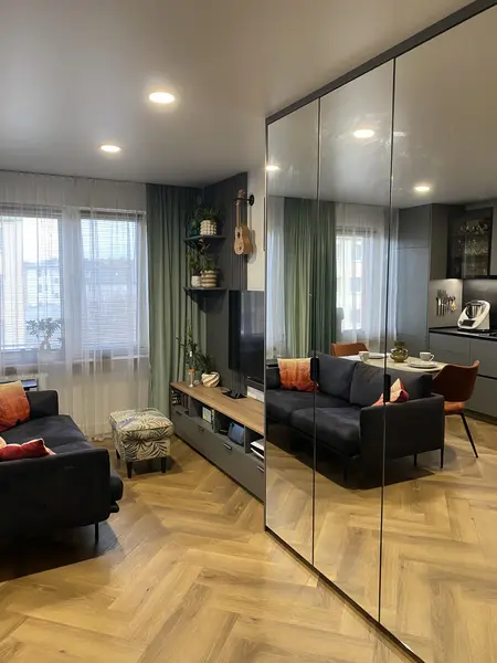 Nowoczesny salon z czarną sofą, drewnianą podłogą i roślinami.