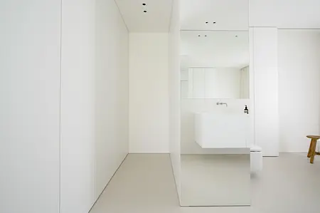 Minimalistyczna łazienka z białą umywalką, lustrem i jasną podłogą.
