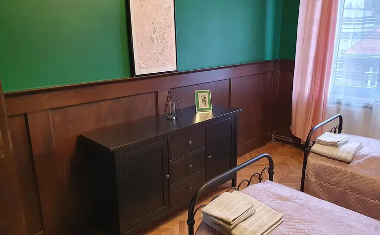 Tradycyjny pokój z zieloną ścianą, drewnianymi meblami i różowymi kołdrami.