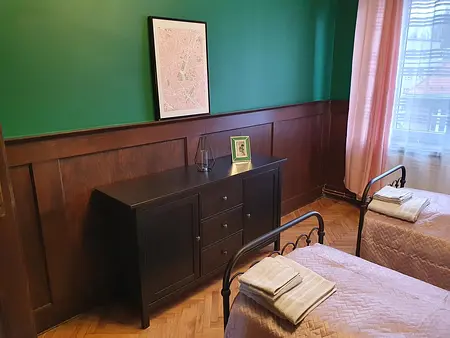 Tradycyjny pokój z zieloną ścianą, drewnianymi meblami i różowymi kołdrami.