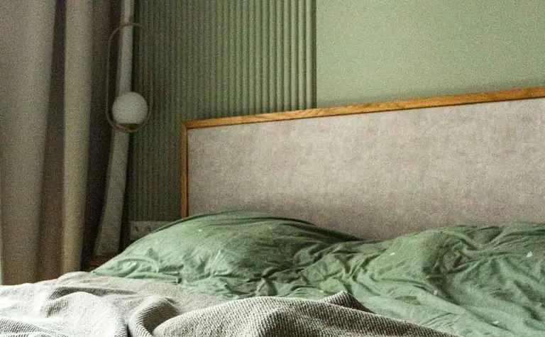 Wnętrze sypialni z zielonymi ścianami i łóżkiem w stylu soft minimalizm.