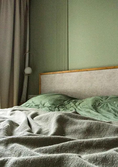 Wnętrze sypialni z zielonymi ścianami i łóżkiem w stylu soft minimalizm.
