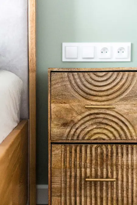 Stylowe wnętrze sypialni z drewnianą szafką i zieloną ścianą, elementy soft minimalizmu.