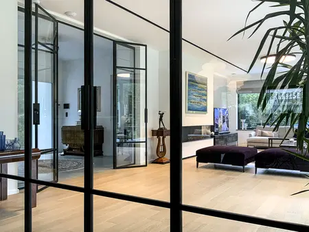 Wnętrze salonu minimalistycznego z dużymi oknami, drewnianą podłogą i roślinnością. Styl minimaluxe, quiet luxury.