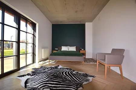 Wnętrze sypialni z zielonym łóżkiem, drewnianymi elementami i industrialnym stylem.