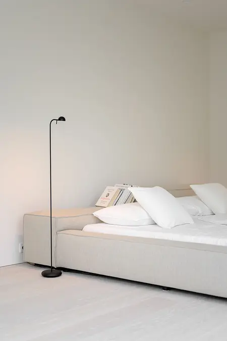 Minimalistyczna sypialnia z szarym łóżkiem, białymi poduszkami i lampą.