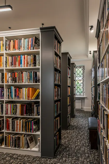 Wnętrze biblioteki z dużymi regałami, tradycyjny styl, książki na półkach, wygodne miejsce do czytania.