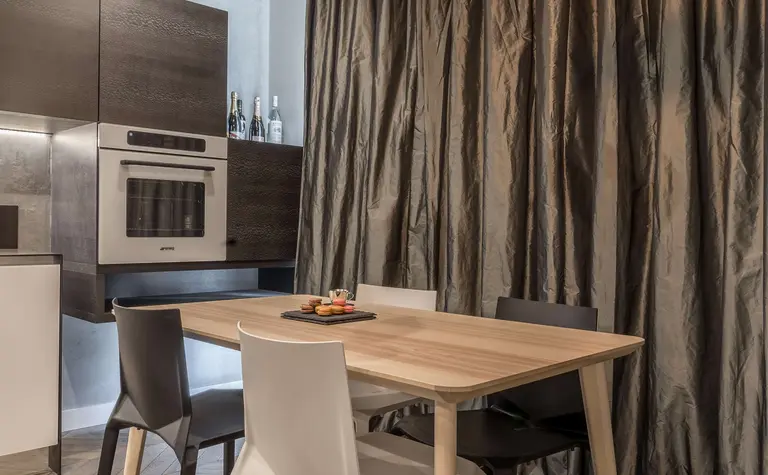 Nowoczesna kuchnia z drewnianym stołem i eleganckimi lampami wiszącymi, ciemnymi szafkami.