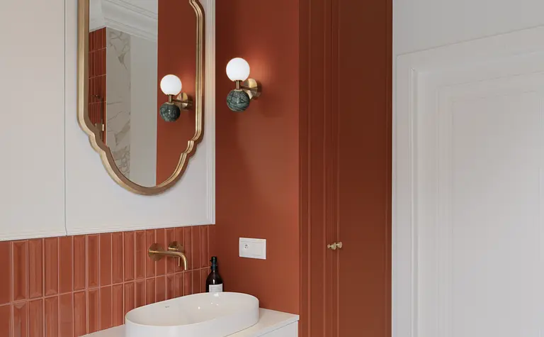 Wnętrze łazienki z pomarańczowymi ścianami, białą umywalką i lustrem w złotej ramie, styl eklektyczny, vintage.