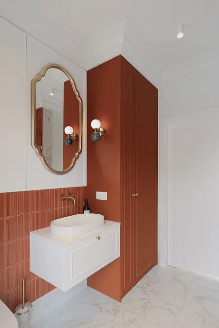 Wnętrze łazienki z pomarańczowymi ścianami, białą umywalką i lustrem w złotej ramie, styl eklektyczny, vintage.