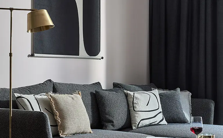 Wnętrze nowoczesnego salonu z szarym sofa, dekoracyjnymi poduszkami i stylowym oświetleniem.