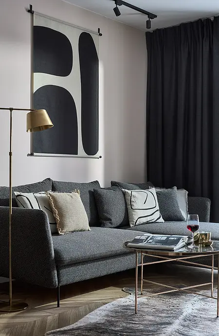 Wnętrze nowoczesnego salonu z szarym sofa, dekoracyjnymi poduszkami i stylowym oświetleniem.