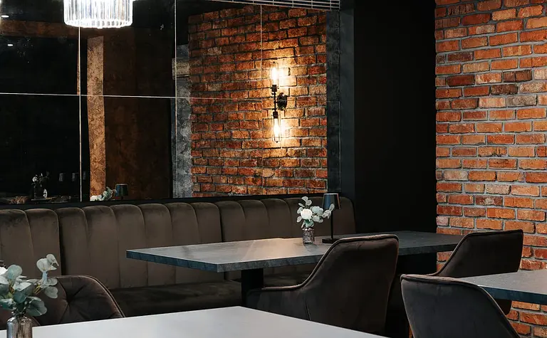 Wnętrze restauracji z ceglaną ścianą, eleganckimi meblami i industrialnym oświetleniem.