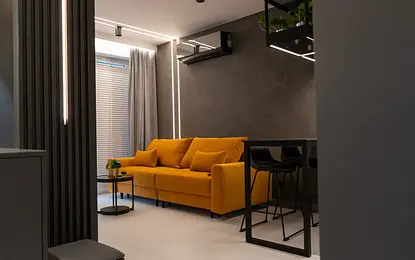 Wnętrze nowoczesnego salonu z żółtą sofą i szarymi ścianami.