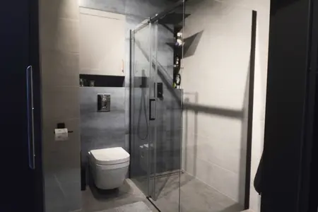 Wnętrze łazienki z minimalistycznym designem, szarymi płytkami i przezroczystą kabiną prysznicową.