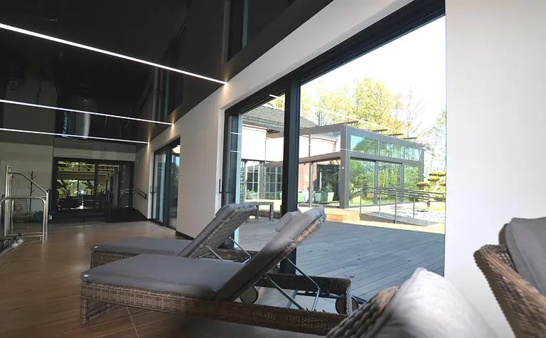 Wnętrze nowoczesnego pomieszczenia z leżakami, dużymi oknami i minimalistycznym designem.