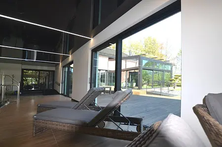 Wnętrze nowoczesnego pomieszczenia z leżakami, dużymi oknami i minimalistycznym designem.
