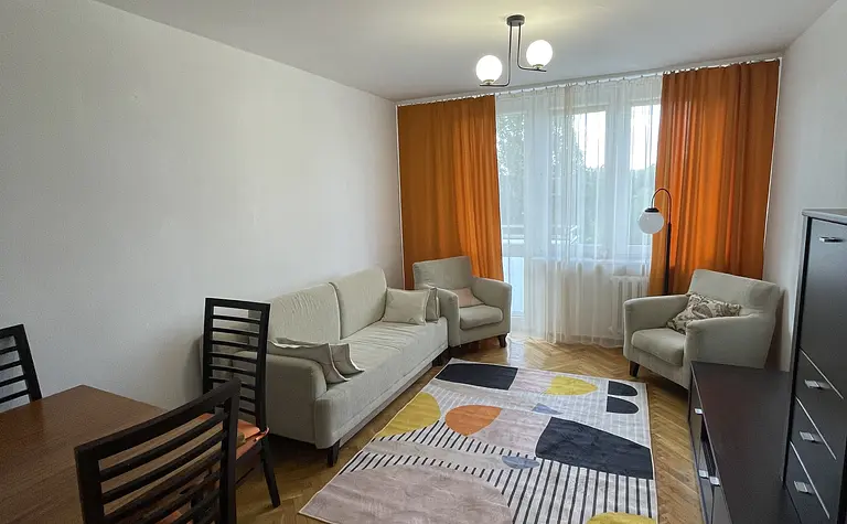 Wnętrze salonu z beżowymi meblami, pomarańczowymi zasłonami i kolorowym dywanem.