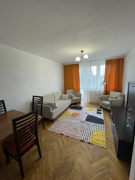 Wnętrze salonu z beżowymi meblami, pomarańczowymi zasłonami i kolorowym dywanem.
