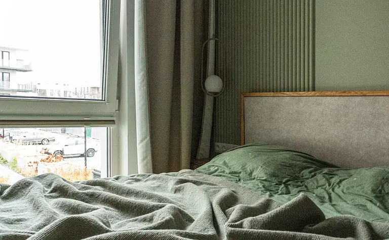 Wnętrze sypialni w stylu nowoczesnym i soft minimalizm z zieloną pościelą.
