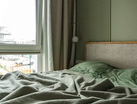 Wnętrze sypialni w stylu nowoczesnym i soft minimalizm z zieloną pościelą.