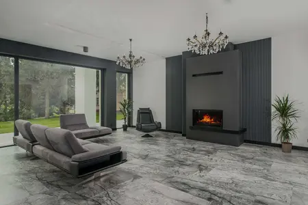 Wnętrze salonu z kominkiem, szarymi meblami i nowoczesnym oświetleniem.