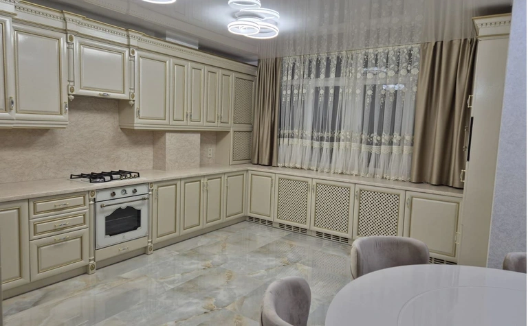 Kuchnia z jasnymi meblami, marmurową podłogą i zasłonami w stylu quiet luxury.