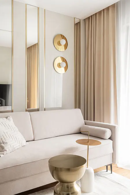 Wnętrze nowoczesnego salonu z jasnym sofą i złotym stolikiem.