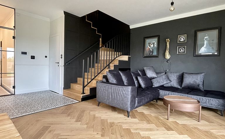 Wnętrze salonu w stylu art deco, industrialnym i vintage z ciemnymi ścianami i drewnianą podłogą.