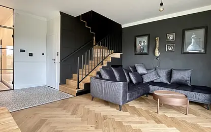 Wnętrze salonu w stylu art deco, industrialnym i vintage z ciemnymi ścianami i drewnianą podłogą.